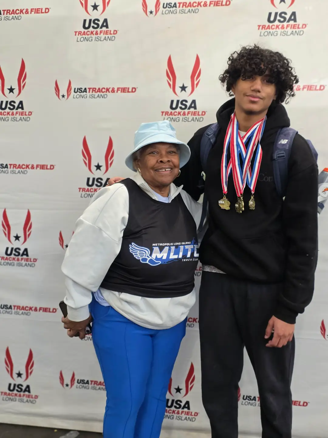 Metropolis athlete Jacob Gallo wearing four medals on ribbons, standing with Coach Ella Williams in front of a USA Track & Field Long Island backdrop.